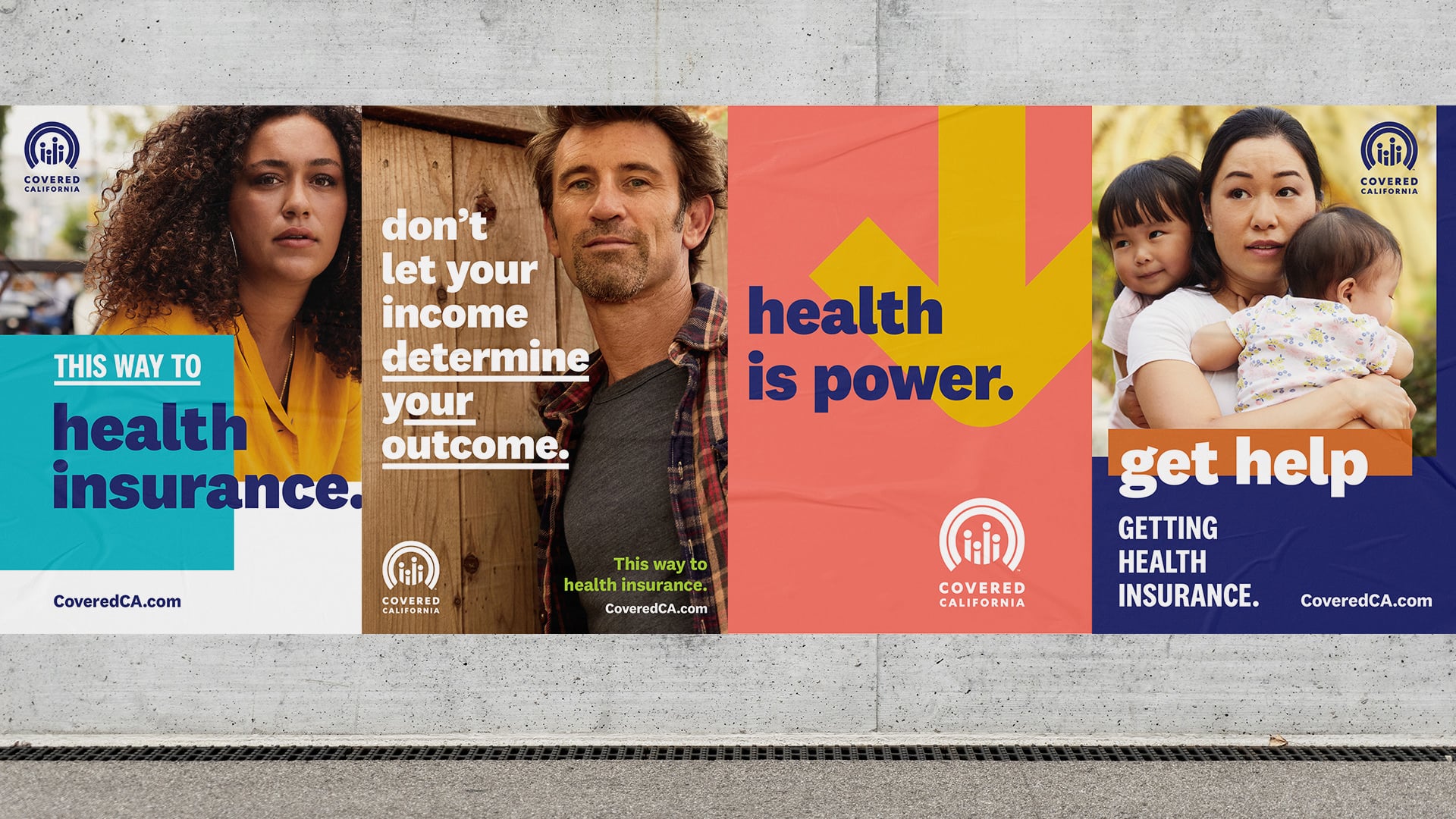 4 posters on a cement wall. Left to right: 1) female-presenting person with long curly brown hair wearing yellow shirt. Text reads "This way to health insurance." 2) Male-presenting person with short brown hair and whisker scruff, text reads "don't let your income determine your outcome." 3) Pink and yellow graphic with arrow that reads "health is power." 4) Female-presenting person holding two children. Text reads "get help getting health insurance." The Covered California logo appears throughout.