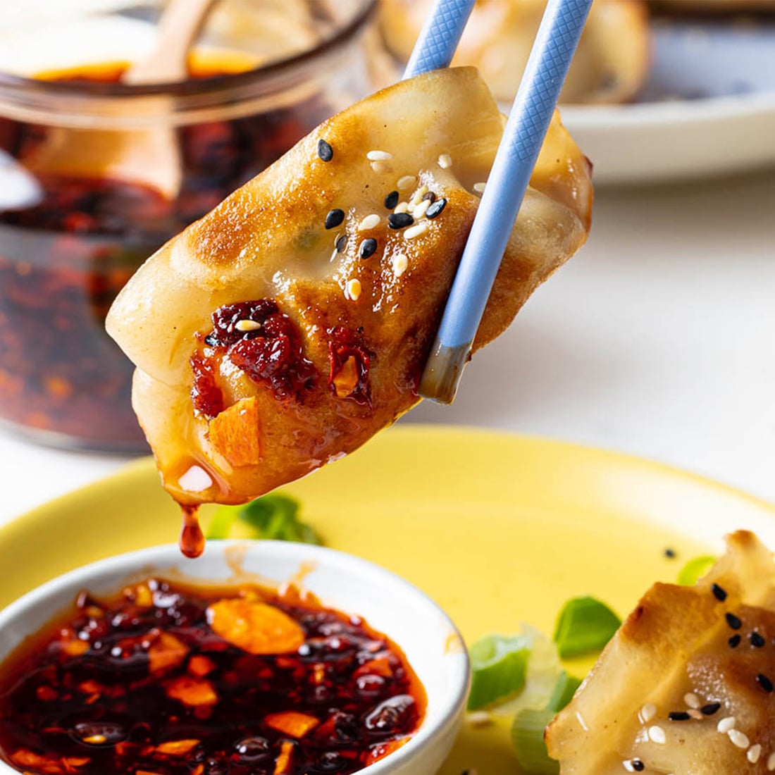 A super close up of a crispy InnovAsian Potsticker being dipped into a spicy chili sauce.
