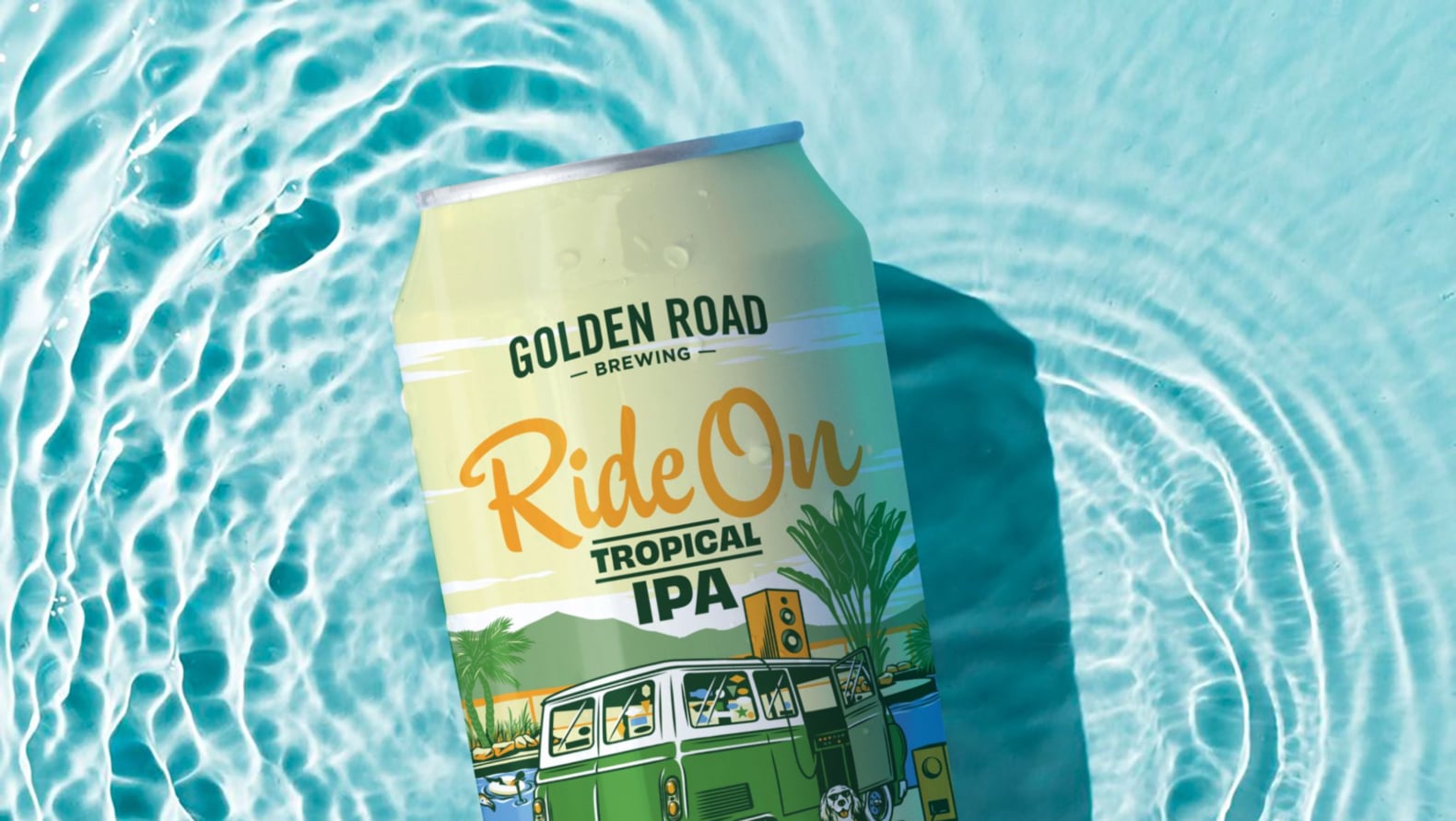 A Golden Road beer can lays in a pool of water. The can is greenish yellow with an illustration of a vintage green van parked next to a pool. The van has vintage speakers attached to its radio. A dog sits next to the van, implausibly wearing sunglasses and a Hawaiian shirt. The beer name "Ride On Tropic IPA" is shown in playful orange script and dark green block letters.