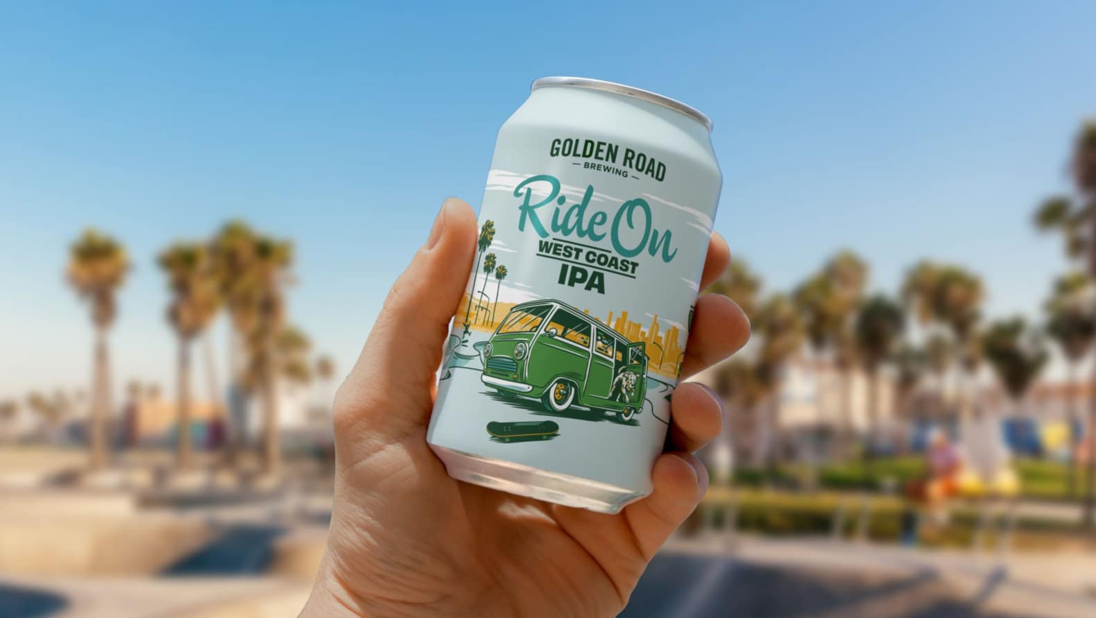 A hand holds a can of Golden Road beer against an out-of-focus background of Venice Beach. The can is light blue with an illustration of a vintage green van parked in front of a skate park with palm trees and a city skyline in the background. A dog leaps from the van toward a dark green skateboard. The beer name "Ride On West Coast IPA" is shown in dark aqua script and dark green block letters.