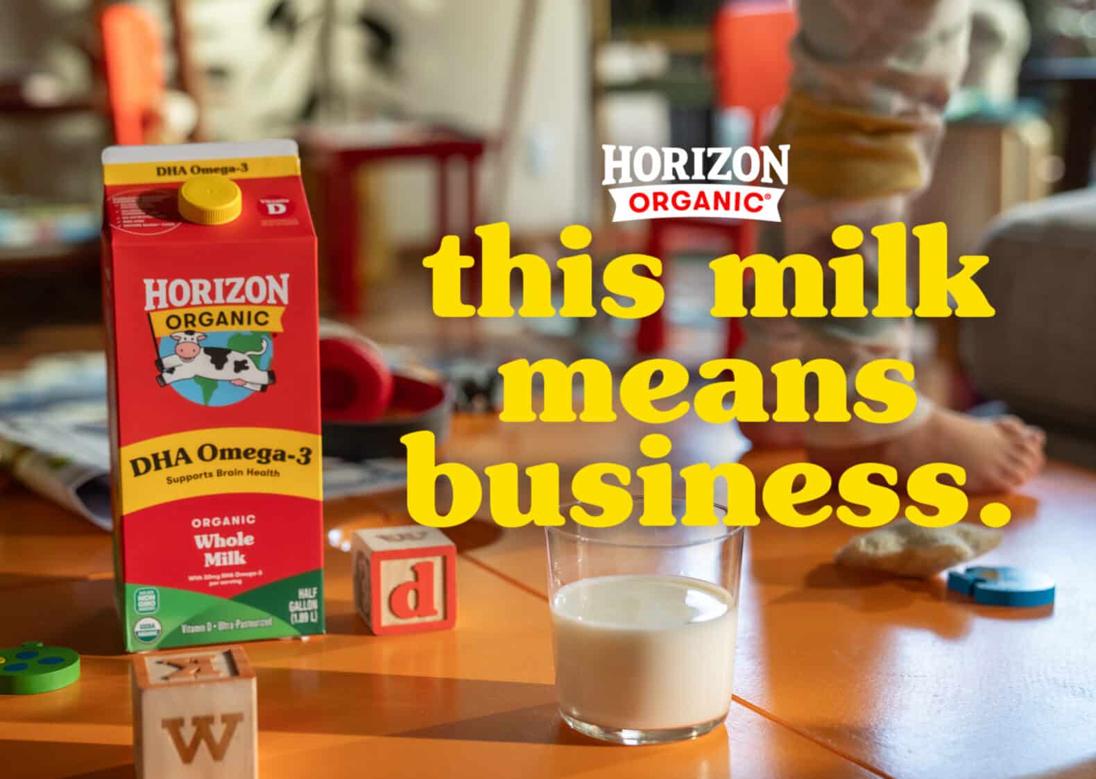 A half gallon of Horizon Organic whole milk sits on a living room coffee table next to a half-full glass of milk and a few children’s alphabet blocks. The campaign line, “this milk means business” is the headline, below the Horizon Organic logo. Behind the type we see a child’s feet; she’s standing on the table.