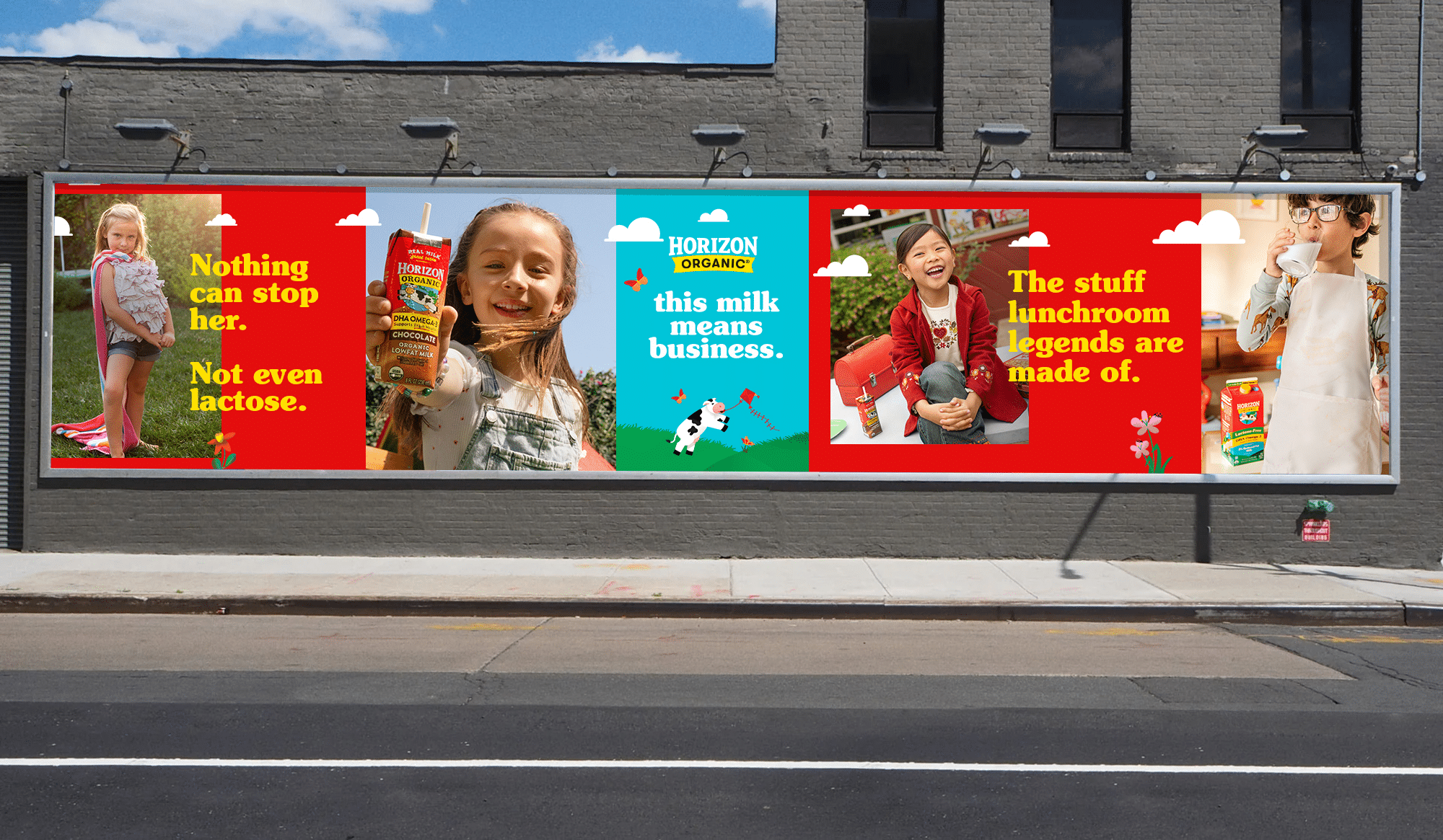 A street scene featuring several campaign posters in a row on a city wall. From the left: a young girl of about 6 years old with blonde hair wearing a towel tied around her neck as a makeshift cape with a sassy look in her eye, standing in a backyard. The headline reads:"Nothing can stop her. Not even lactose." Next poster: an 8-year-old girl with light brown hair holding container of Chocolate Milk. camera. Next: An illustrated image of Happy the Cow, the Horizon Organic brand mascot, as she flies a kite. The headline reads:"this milk means business." Next poster: an elementary-school-aged laughing girl with brown hair and a bright red blazer. next to her is a red lunchbox and Chocolate Milk. The headline reads: "The stuff lunchroom legends are made of." And the final poster features a boy wearing an apron over his jammies and drinking a glass of milk.