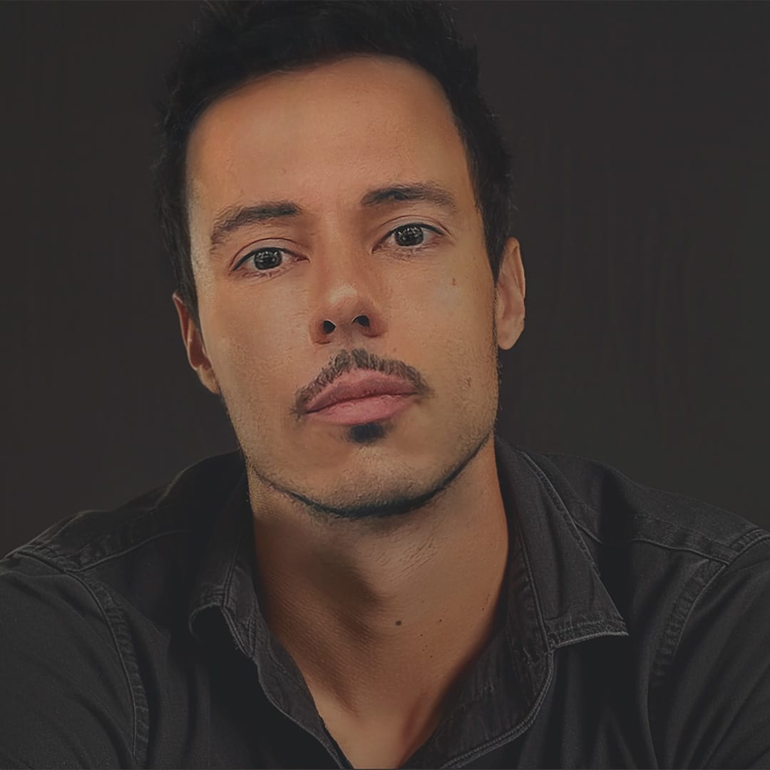 Portrait of a person with short dark hair and anchor beard mustache. They stare into the camera thoughtfully.